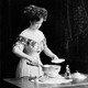 A model demonstrates a newfangled electric chafing dish, ca. 1910